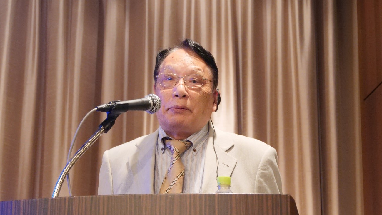 カーテンの前にいるスーツを着た男性自動的に生成された説明