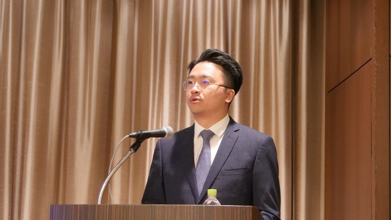 カーテンの前に立っているスーツを着た男性中程度の精度で自動的に生成された説明